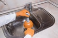 WomanÃ¢â¬â¢s hands with orange gloves cleaning sewer at kitchen faucet over metal sink. Closeup of hand with plunger Royalty Free Stock Photo